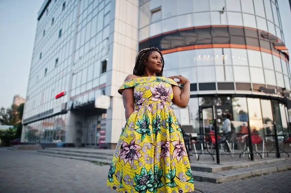 Sevimli küçük yükseklik Afro-Amerikan Kız dreadlocks, bina büyük pencereler karşı yöneltilen renkli sarı elbise giymek.