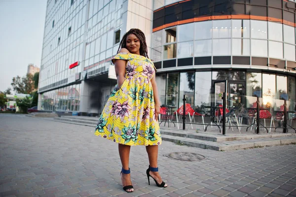 Sevimli küçük yükseklik Afro-Amerikan Kız dreadlocks, bina büyük pencereler karşı yöneltilen renkli sarı elbise giymek.