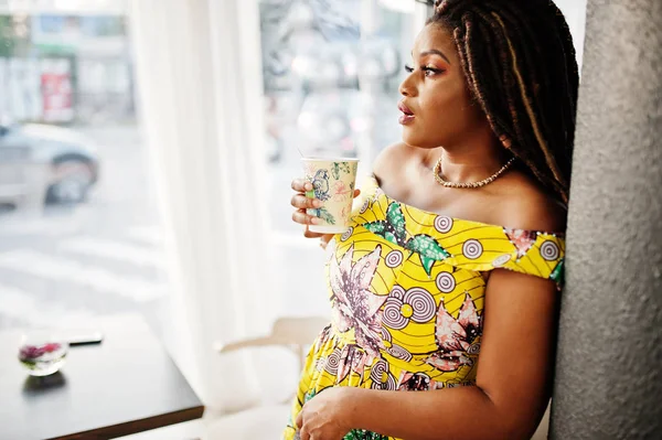 Sevimli küçük yükseklik dreadlocks, Afrikalı-Amerikalı kızla kafede kahve ile poz renkli sarı elbise giymek.