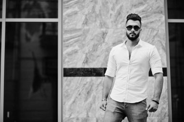 Şık uzun Arap adam modelinde beyaz gömlek, kot pantolon ve güneş gözlüğü şehir Caddesi'nde poz verdi. Sakal çekici Arap adam.