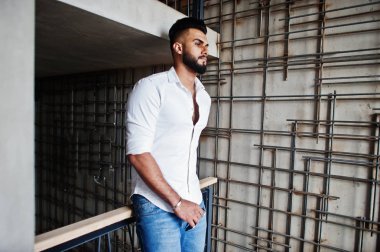 Şık uzun Arap adam modelinde beyaz gömlek, kot çelik duvara kapalı poz verdi. Sakal çekici Arap adam.