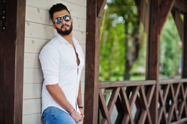 Şık uzun Arap adam modelinde beyaz gömlek, kot pantolon ve güneş gözlüğü şehir Caddesi'nde poz verdi. Sakal çekici Arap adam.