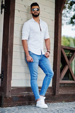 Şık uzun Arap adam modelinde beyaz gömlek, kot pantolon ve güneş gözlüğü şehir Caddesi'nde poz verdi. Sakal çekici Arap adam.