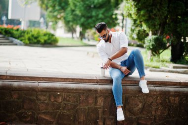 Şık uzun Arap adam modelinde beyaz gömlek, kot pantolon ve şehir Caddesi'nde oturan güneş gözlüğü. Kahve Park'ta sakal çekici Arap adamla.