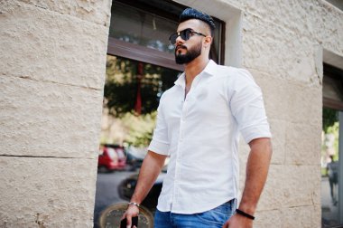 Şık uzun Arap adam modelinde beyaz gömlek, kot pantolon ve güneş gözlüğü şehir Caddesi'nde poz verdi. Sakal çekici Arap adam.