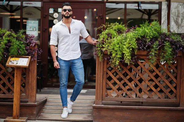 Şık uzun Arap adam modelinde beyaz gömlek, kot pantolon ve güneş gözlüğü şehir Caddesi'nde poz verdi. Sakal çekici Arap adam.