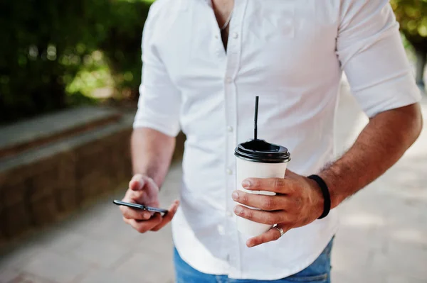 Close up photo of guy with cup of coffee and mobile phone at hands.