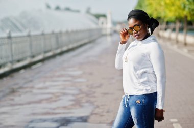 Güneş gözlüğü, siyah Tesettür, beyaz tişört ve kot Afrika Müslüman kız çeşme karşı açık poz verdi.