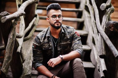 Harika güzel uzun boylu ararbian sakal maço erkek gözlük ve askeri ceket ahşap merdiven karşı açık poz verdi.