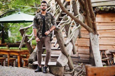 Harika güzel uzun boylu ararbian sakal maço erkek gözlük ve askeri ceket ahşap merdiven karşı açık poz verdi.