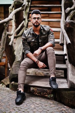Harika güzel uzun boylu ararbian sakal maço erkek gözlük ve askeri ceket ahşap merdiven karşı açık poz verdi.