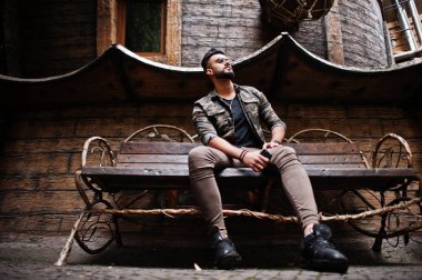 Ahşap ev karşı bankta oturmuş müthiş güzel uzun boylu ararbian sakal maço erkek gözlük ve askeri ceket açık, poz verdi.