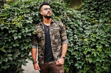 Harika güzel uzun boylu ararbian sakal maço erkek gözlük ve askeri ceket açık yeşil yaprakları kemer karşı yöneltilen.