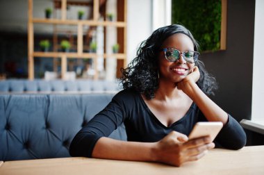 Afro-Amerikan Kız kafede oturan ve cep telefonu el altında tutan güneş gözlüğü.