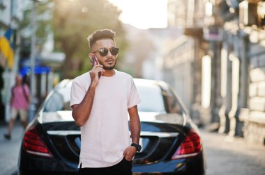 Güneş gözlüğü ve lüks araba ve cep telefonu konuşma karşı pembe tişört şık Hint sakallı adam. Hindistan zengin model şehrin sokaklarında, açık poz verdi.