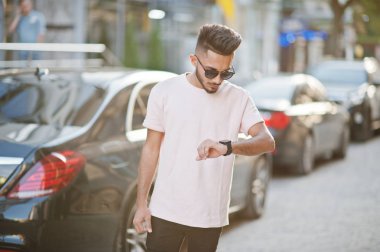 Güneş gözlüğü ve lüks otomobil karşı pembe tişört şık Hint sakallı adam. Hindistan zengin model sokakları şehir ve onun saatler seyir, açık poz verdi.