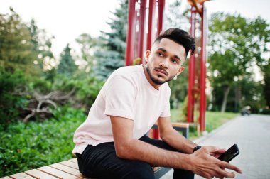 Pembe tişört şık Hint sakallı adam. Hindistan şehir bankta oturan model ve cep telefonunu kullanma.