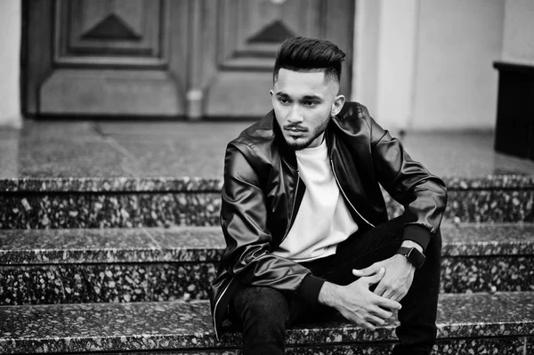 Stylish indian beard man at black leather jacket. India model posed sitting at streets of city.