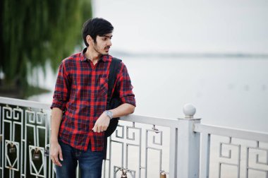 Akşam şehre karşı göl üzerinde kareli gömlek ve sırt çantası ile kot Genç Hintli öğrenci adama poz.