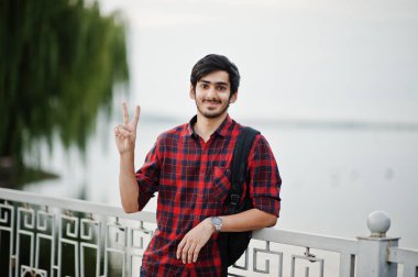 Kareli gömlek ve kot üzerinde akşam şehre Gölü karşı yöneltilen sırt çantası ile genç Hintli öğrenci adama iki parmak gösterir.