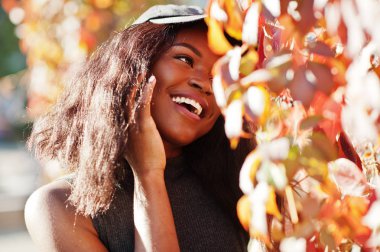 Şapkalı şık Afro-Amerikan kız kırmızı yaprakları karşı güneşli sonbahar günü, poz verdi. Afrika model kadın.