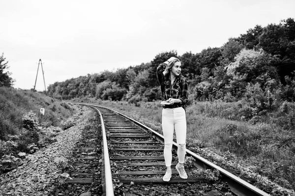 Portrait of a pretty blond girl in tartan shirt walking on the railway with map in her hands.