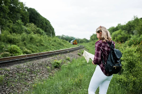 Portrait of a young blonde in tartan shirt next to the train with a map.