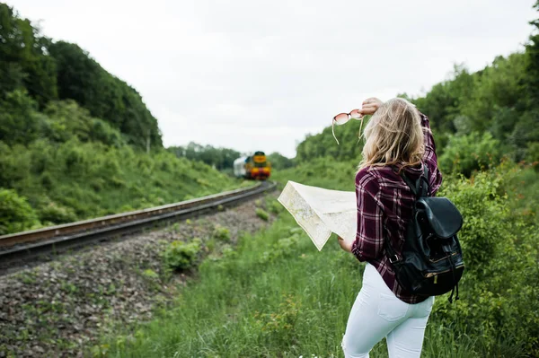 Portrait of a young blonde in tartan shirt next to the train with a map.