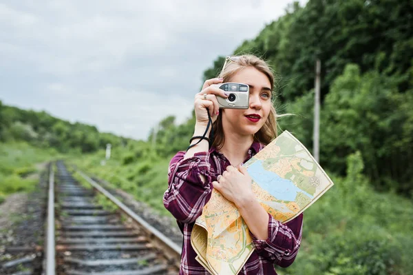 Portrait of a gorgeous young girl in tartan shirt taking pictures with camera on the railway.