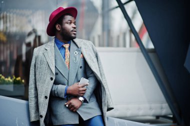 Şık Afro-Amerikan man modeli gri ceket, ceket kravat ve elinde cep telefonu ile kırmızı şapka.