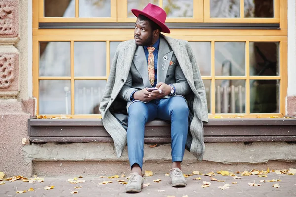 灰色でスタイリッシュなアフリカ系アメリカ人モデルのコート ジャケット ネクタイと赤い帽子に対して大きな窓に座って 携帯電話を手で保持 — ストック写真