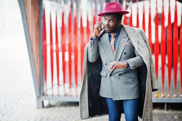 グレーのコート ジャケット ネクタイ 赤い背景カフェ 時計を見て 携帯電話で話すに対して提起赤い帽子でスタイリッシュなアフリカ系アメリカ人モデル — ストック写真