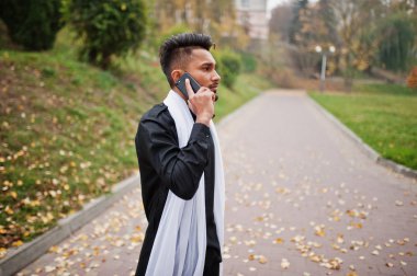 Açık ve cep telefonuyla konuşan şık Hintli beyaz kaşkollu ile siyah geleneksel giysiler içinde poz.