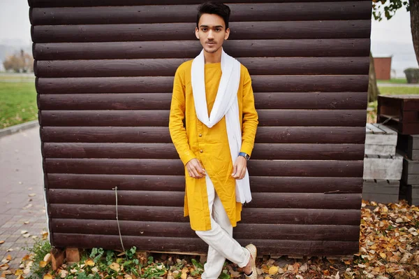 白いスカーフで黄色の伝統的な服でインドのスタイリッシュな男が屋外木製の背景に対してもたらされる — ストック写真