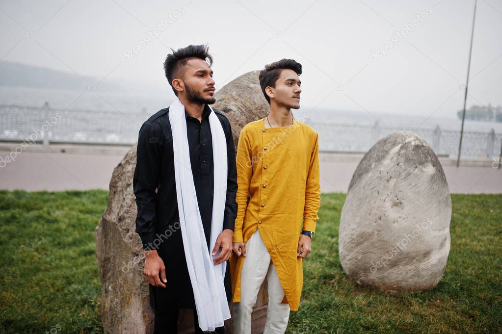 Two indian stylish mans friends in traditional clothes posed outdoor against big stones.