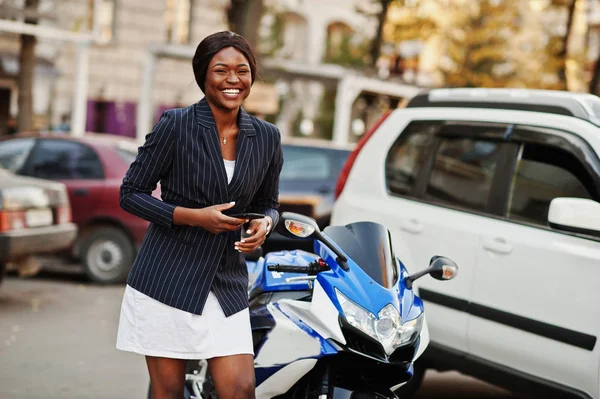 Success stylish african american woman with phone at hands against motorcycle.