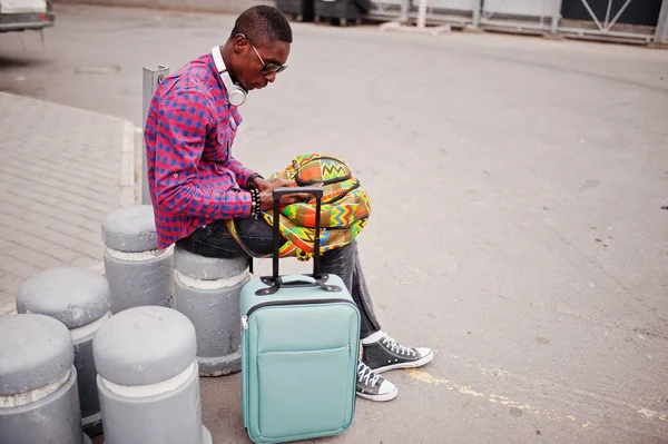 格子縞のシャツ サングラス スーツケースとバックパックのイヤホンでアフリカ系アメリカ人 携帯電話を手で保持している黒人男性旅行者 — ストック写真