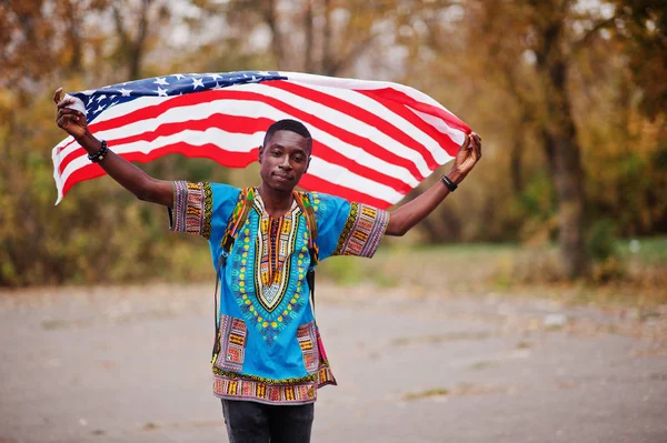 African man in africa traditional shirt on autumn park with USA flag.
