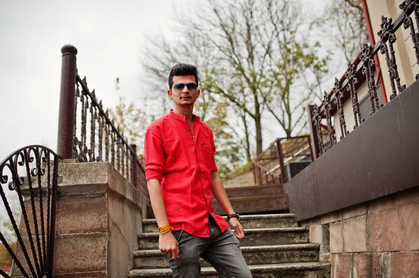 Indian man at red shirt and sunglasses posed outdoor.