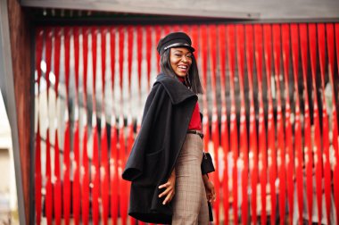 Street kırmızı bir arka plan karşı yöneltilen ceket ve gazeteci çocuk şapkalı kız Afro-Amerikan moda.