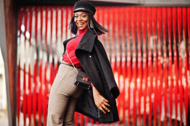 Street kırmızı bir arka plan karşı yöneltilen ceket ve gazeteci çocuk şapkalı kız Afro-Amerikan moda.