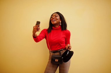 Cep telefonu ile sarı arka plana karşı Afro-Amerikan moda kız haber teIIaIı kap ile poz verdi.