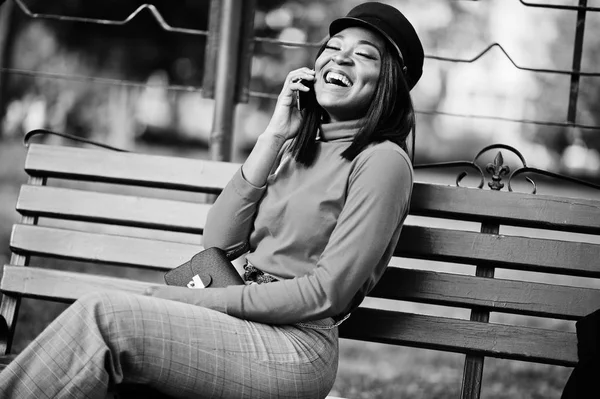 携帯電話でベンチに座って 通りで脅威のハンドバッグで キャスケット キャップのアフリカ系アメリカ人のファッションの女の子 — ストック写真