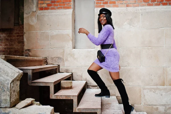 African american woman at violet dress and cap posed outdoor, walking on stairs.