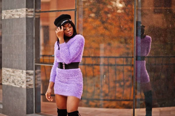 African american woman at violet dress and cap posed outdoor against modern building.