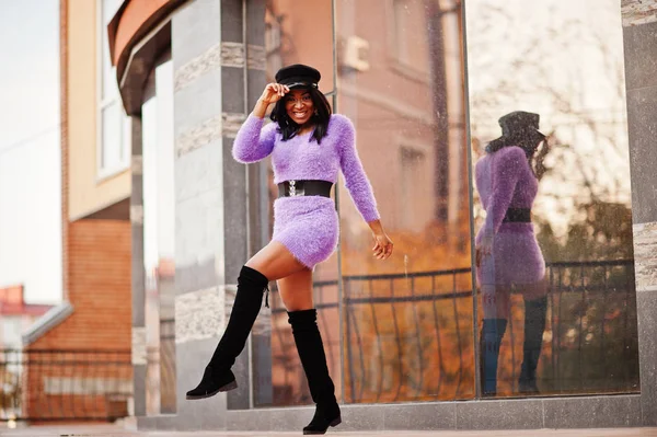 African american woman at violet dress and cap posed outdoor against modern building.