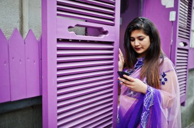 Elinde cep telefonu ile Street mor windows karşı geleneksel violet saree Hint hindu kız poz verdi.