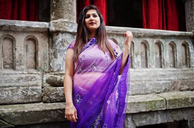 Street kırmızı perdeler ile eski eve karşı geleneksel violet saree Hint hindu kız poz.