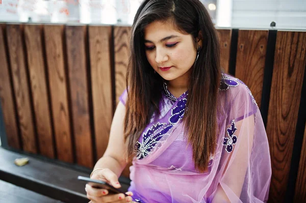 印度印度女孩在传统的紫罗兰色萨里坐在咖啡馆桌旁 手里拿着手机 — 图库照片