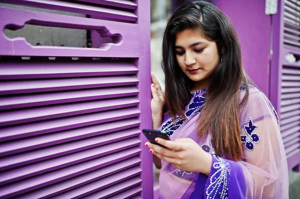 印度印度女孩在传统的紫罗兰色萨里在街上摆出反对紫色的窗户与手机在手 — 图库照片